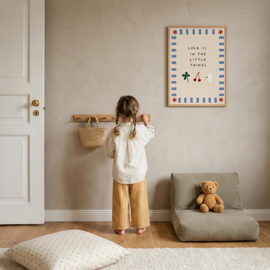 A young girl stands in a cozy room, looking up at a framed poster with a message about luck. The room has a wooden floor, a chair, and a teddy bear on a couch.