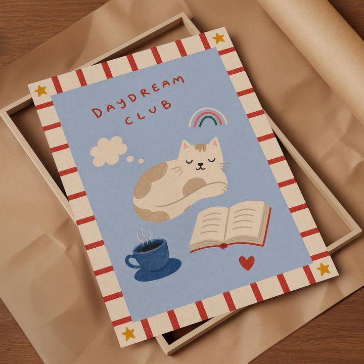 The image is a framed print with a cat sleeping on a blue background, surrounded by various objects such as a cup, a book, and a heart.