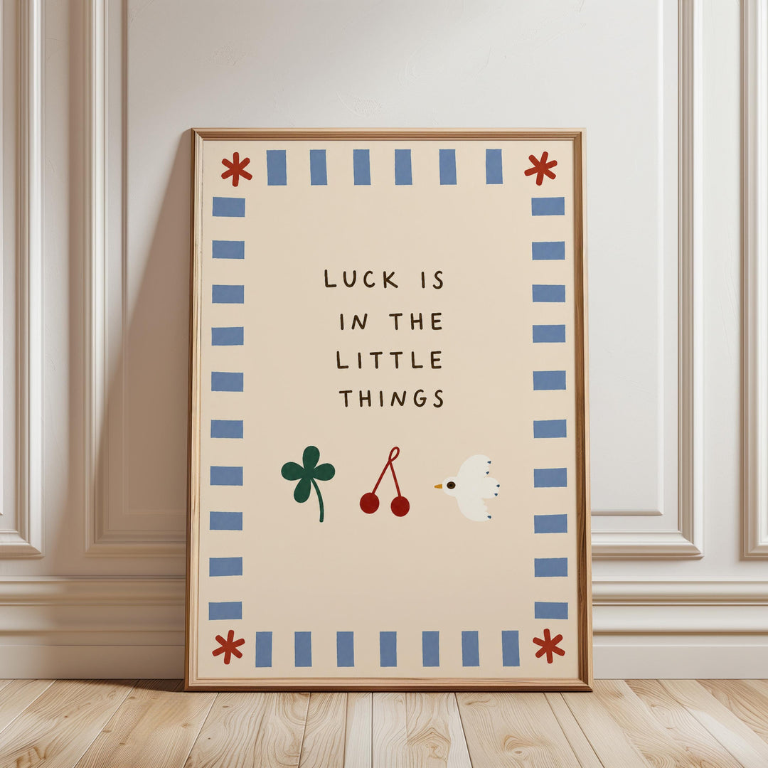 A framed poster with the text "LUCK IS IN THE LITTLE THINGS" and illustrations of a clover, cherries, and a bird.