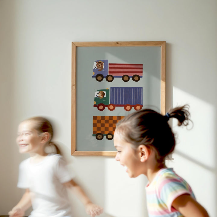 Two young girls are running in a room, with a framed picture of colorful trucks hanging on the wall behind them.