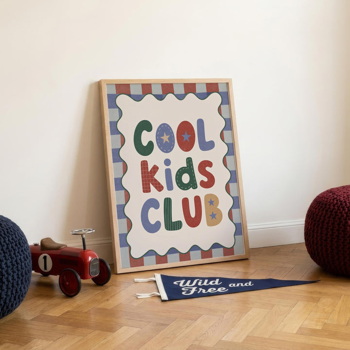 a framed sign that reads "Cool Kids Club" with a decorative border, placed on a wooden floor next to a toy tractor and a blue flag.