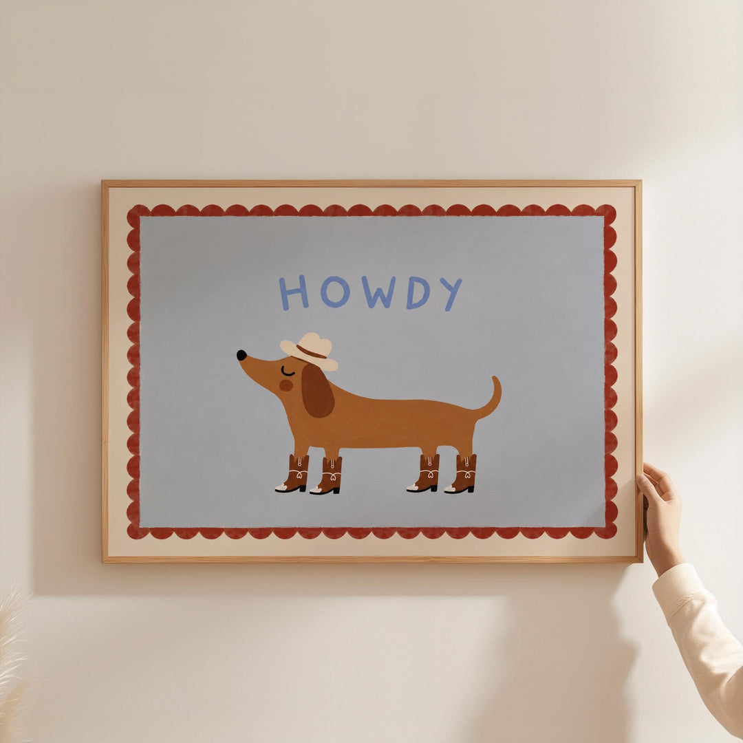 A person is holding a framed picture of a cartoon dog wearing a cowboy hat and boots, with the word "HOWDY" written above it.