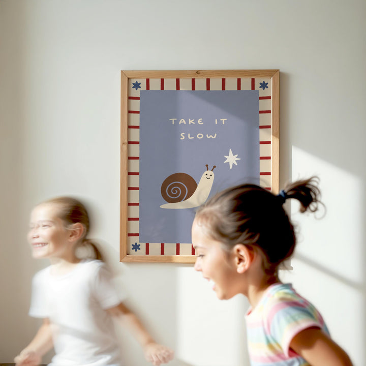 Two young girls are running in a room with a framed poster on the wall that says "TAKE IT SLOW" and features a snail and a star.