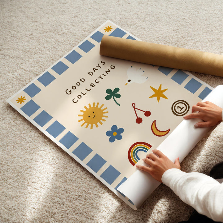 A child's hands are rolling up a poster with various colorful illustrations, including a sun, flowers, and other whimsical designs.