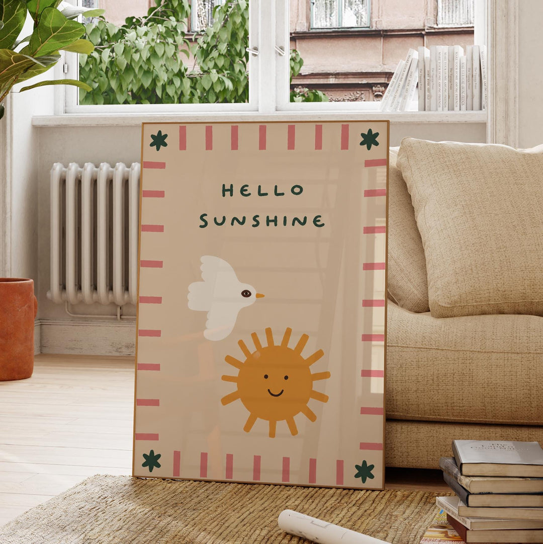 A framed poster with a cheerful design of a bird and a sun, along with the text "Hello Sunshine" is displayed on a wooden floor in a living room.