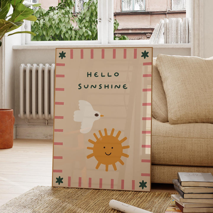 A framed poster with a cheerful design of a bird and a sun, along with the text "Hello Sunshine" is displayed on a wooden floor in a living room.