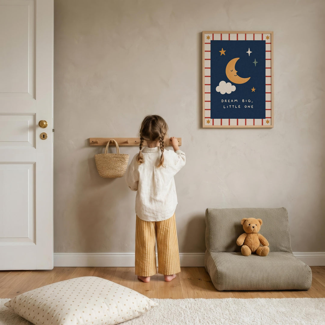 A young girl stands in a cozy room, looking up at a framed picture on the wall. The room has a wooden floor, a chair, and a teddy bear on the floor.