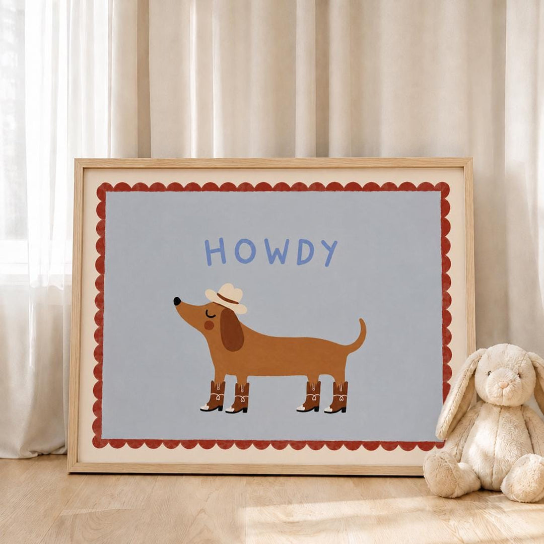 A framed illustration of a cartoon dog wearing a cowboy hat and boots, with the word "HOWDY" written above it, is displayed on a wooden floor next to a stuffed rabbit.
