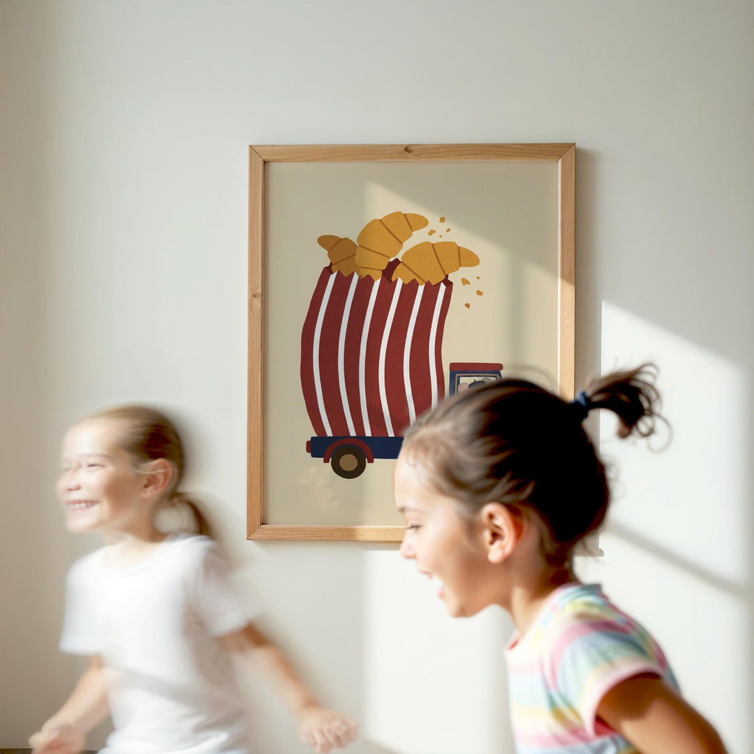Two young girls are running in a room, with a framed picture of a red and white striped cart with a carton of bread on it hanging on the wall behind them.
