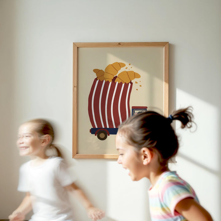Two young girls are running in a room, with a framed picture of a red and white striped cart with a carton of bread on it hanging on the wall behind them.