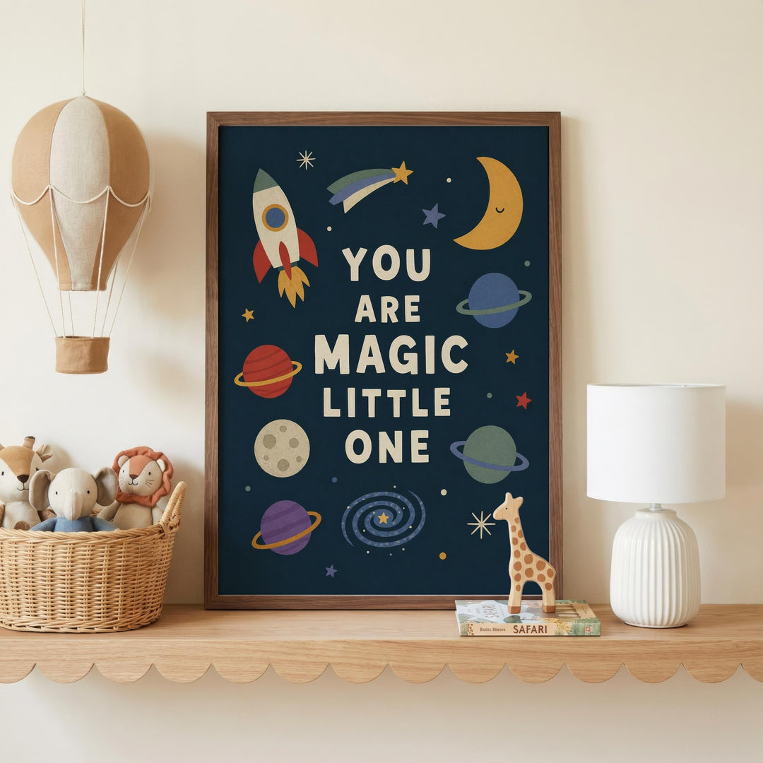 a framed poster with a space-themed design, including a rocket ship, planets, and stars, along with the text "YOU ARE MAGIC LITTLE ONE". The poster is displayed on a shelf, accompanied by a basket of stuffed animals and a lamp.