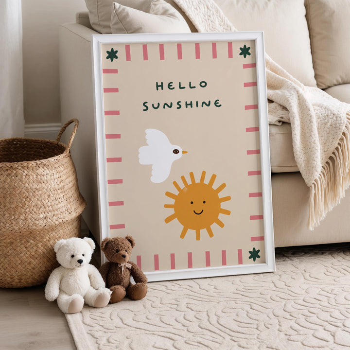 A framed poster with a cheerful design, including a white bird, a yellow sun, and a smiling face, is displayed on a beige couch. Next to the poster are two stuffed animals, one white and one brown.