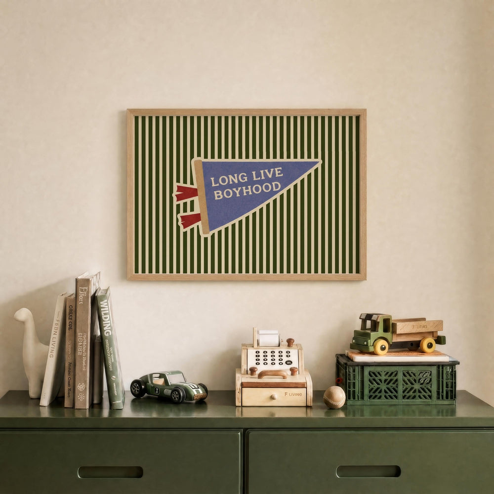 a framed poster with the text "LONG LIVE BOYHOOD" on it, displayed on a wall above a green dresser with various items on it, including books, toys, and a toy car.