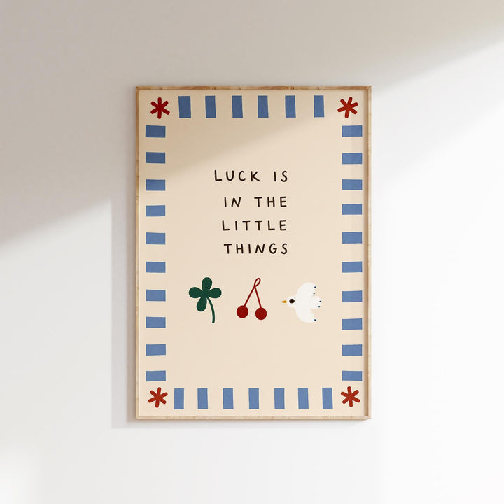 The image is a framed poster with the text "LUCK IS IN THE LITTLE THINGS" and illustrations of a clover, cherries, and a bird.