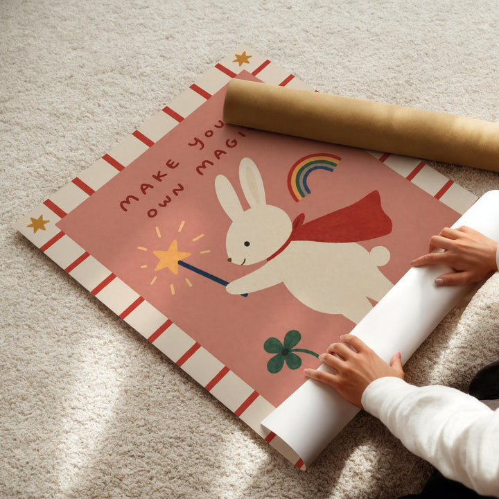 A child's hands are seen rolling up a large poster featuring a cartoon rabbit holding a wand and a rainbow.