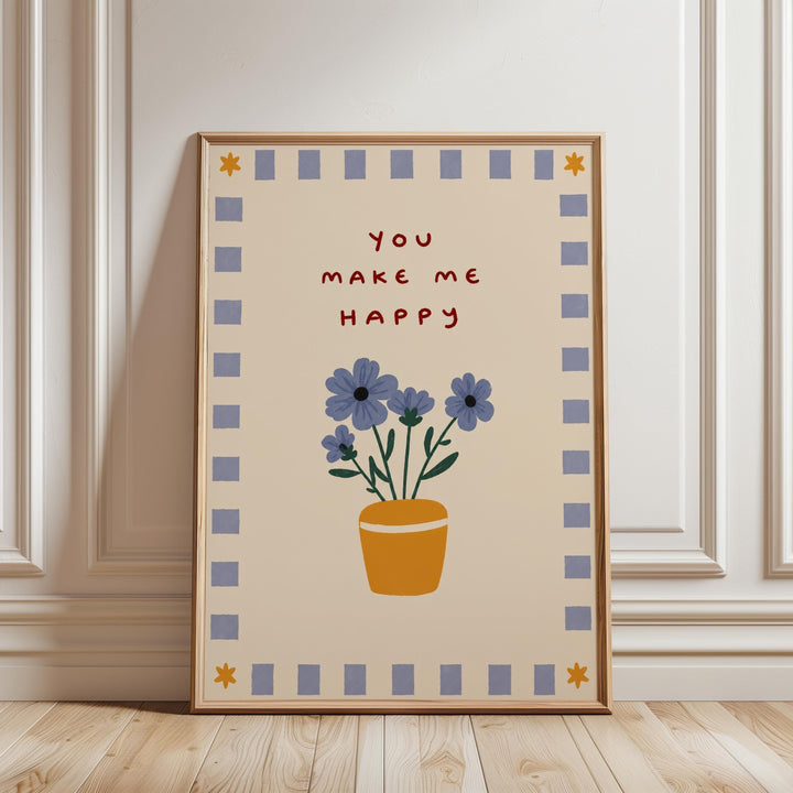 A framed poster with a floral design and the text "You make me happy" on it, placed on a wooden floor against a white wall.