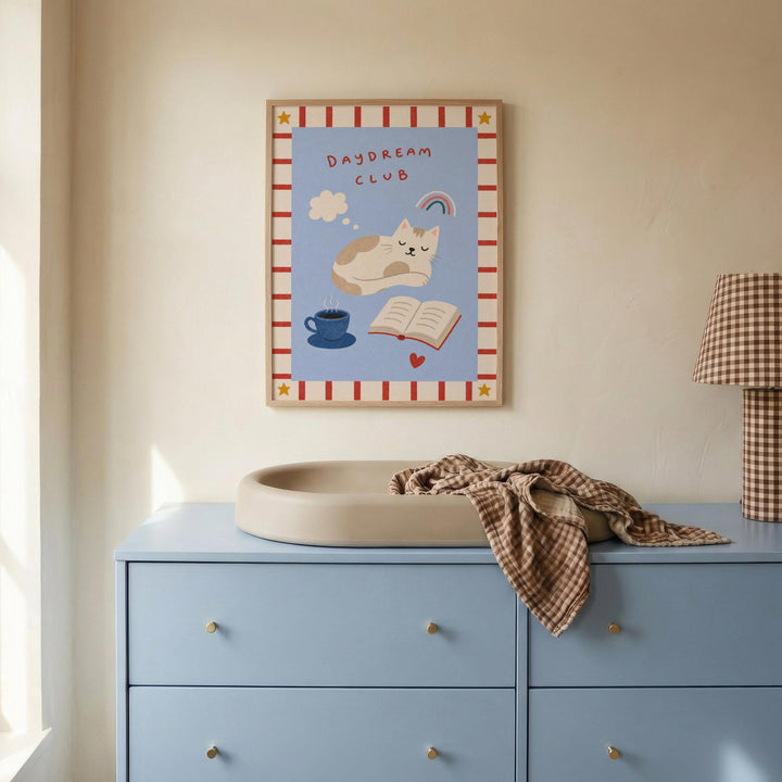 a blue dresser with a white sink, a framed poster of a cat and a book, and a lamp on the dresser.
