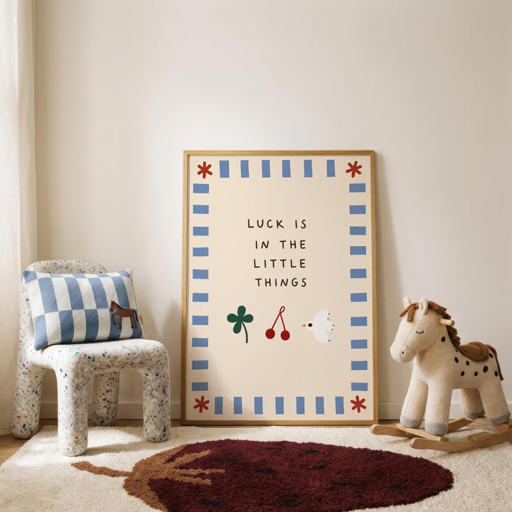 a child's bedroom with a framed poster on the wall that says " Luck is in the little things". Next to the poster is a rocking horse, and there is a checkered chair in the room.