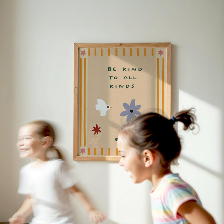 Two young girls are running in front of a framed poster with the text "Be kind to all kinds" and illustrations of flowers and birds.