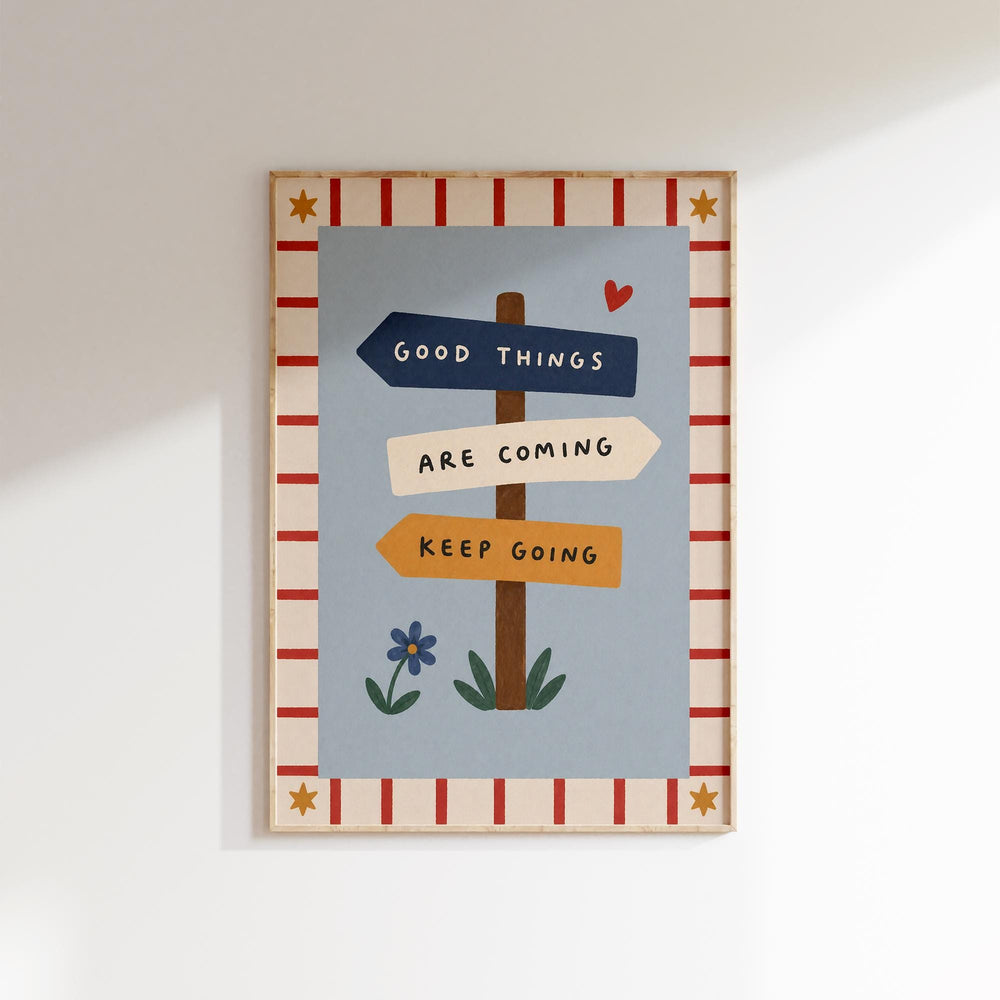 The image is a framed poster with a blue background and a red and white border. The poster features a sign with the text "Good Things Are Coming" and a heart symbol, along with a flower and a star.