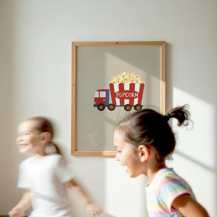 Two young girls are running in a room with a framed picture of a red and white popcorn truck on the wall.