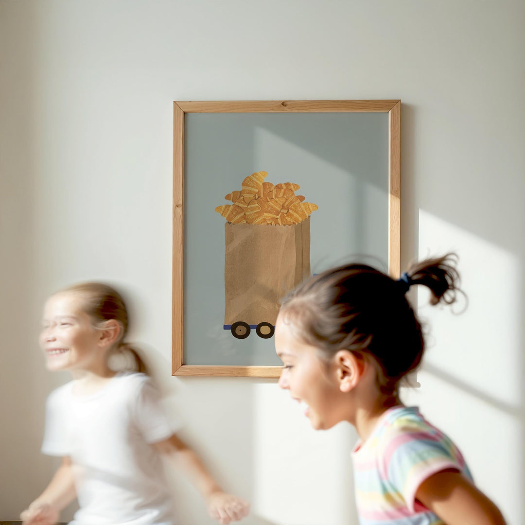 Two young girls are running in front of a framed image of a bag of bread on a wall.