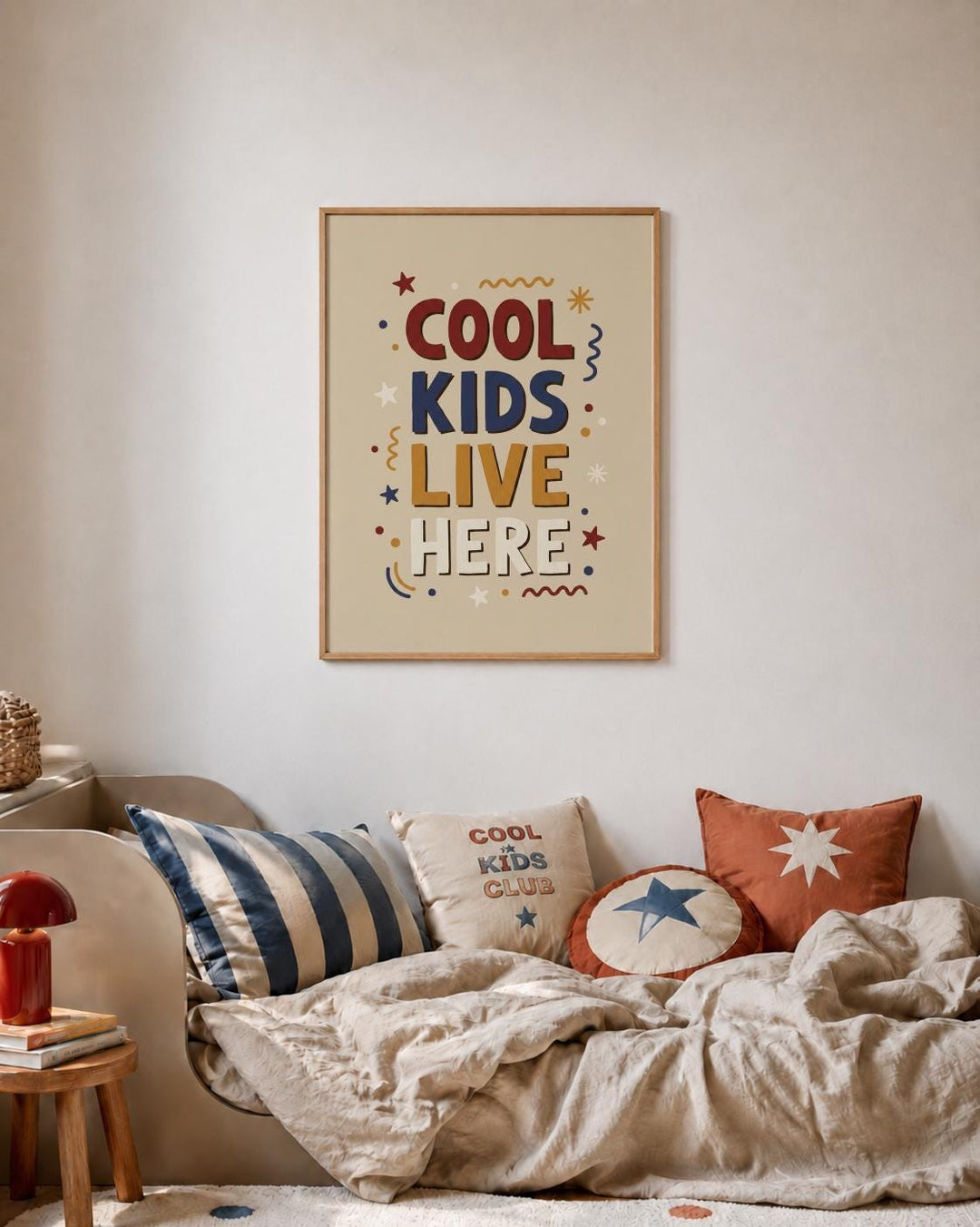a cozy bedroom scene with a framed poster on the wall that reads "COOL KIDS LIVE HERE". The poster is surrounded by various decorative elements, including stars and swirls, creating a playful and vibrant atmosphere. The room also contains a bed with striped pillows and a red lamp, contributing to the overall warm and inviting ambiance.