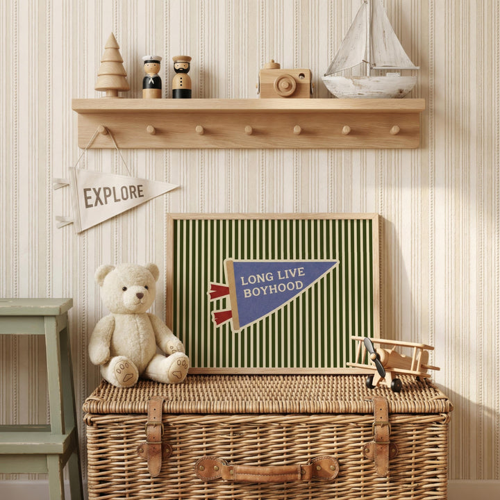 a wooden shelf with various toys and a banner, including a teddy bear, a toy airplane, and a sailboat. The shelf has a wicker basket underneath it, and there is a framed banner with the words "Long Live Boyhood" displayed on it.