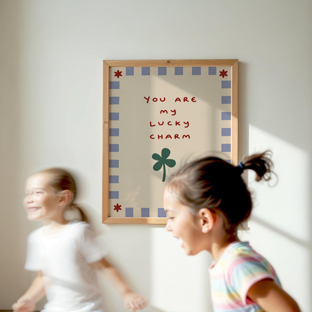 Two young girls are running in front of a framed sign with a message that says "You are my lucky charm".