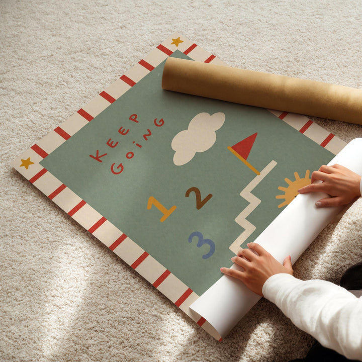 A child's hands are seen rolling up a colorful poster with the text "Keep Going" on it, which appears to be a motivational poster.