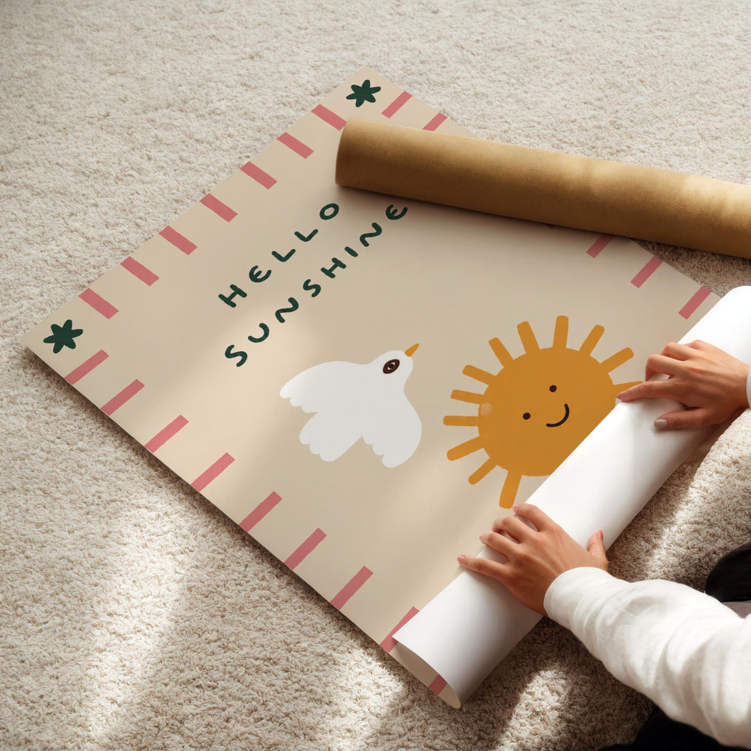A child's hands are seen rolling up a poster with a cheerful design featuring a bird, sun, and text that reads "Hello Sunshine".