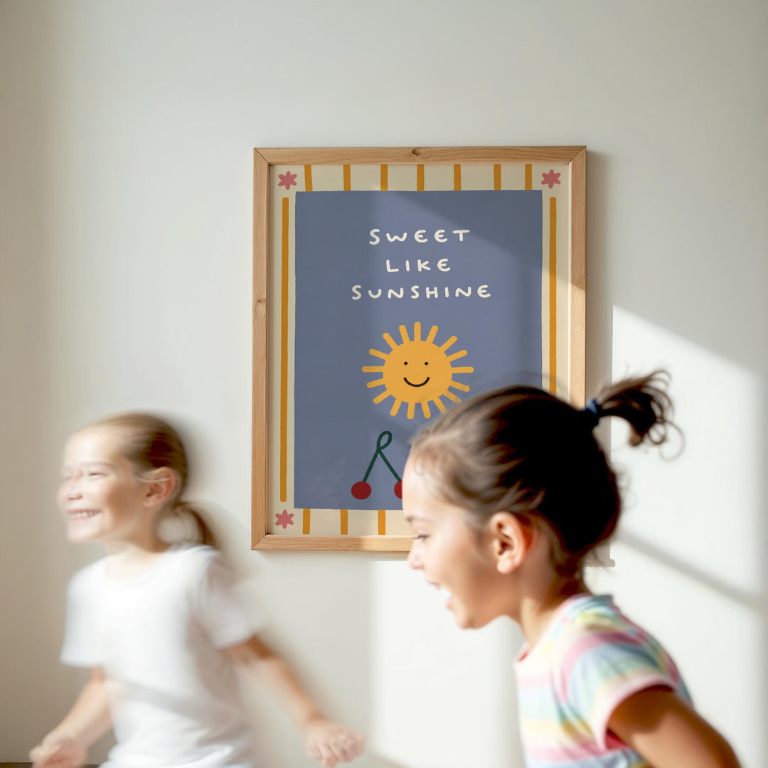 Two young girls are running in front of a framed poster with a cheerful sun and the text "Sweet like sunshine".