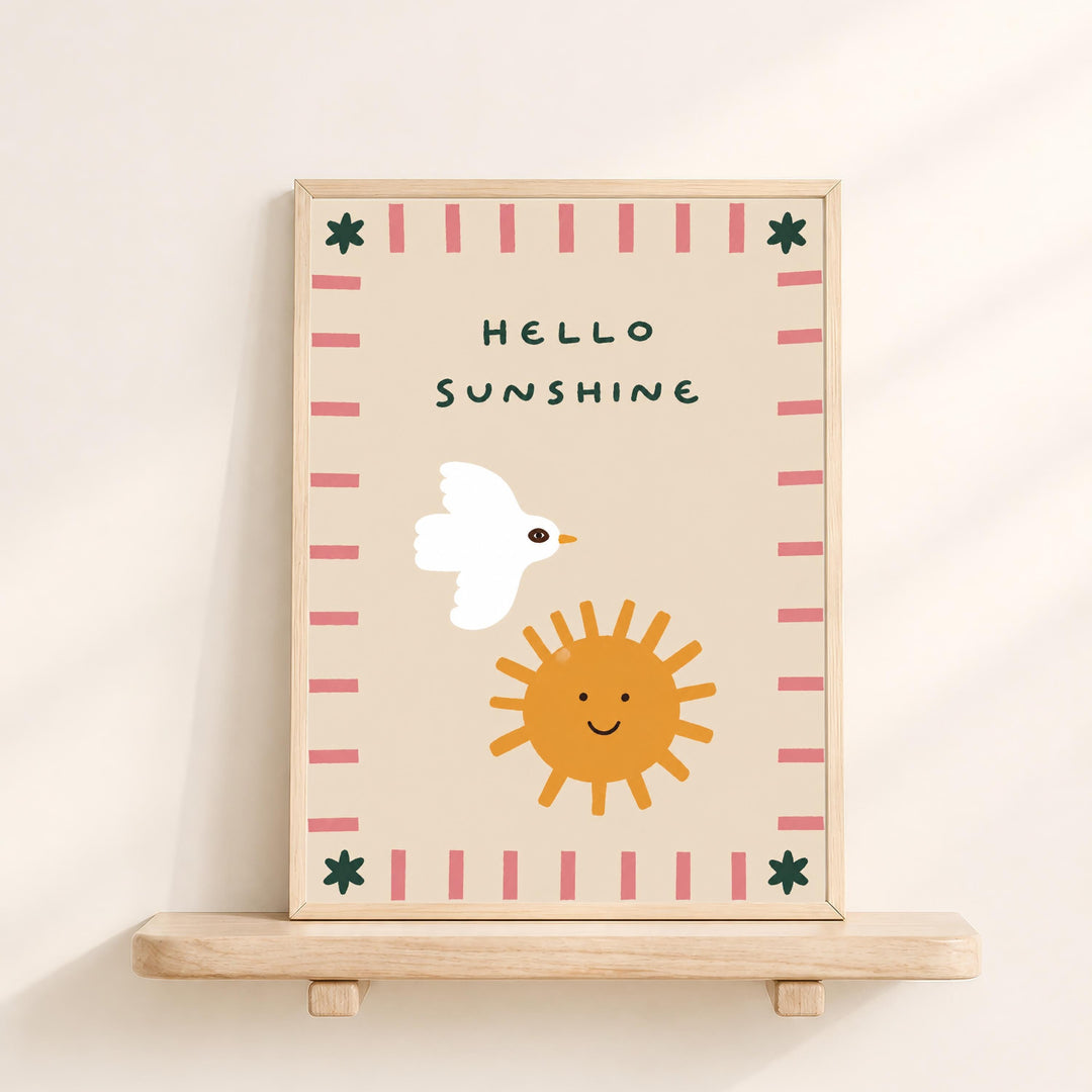 A framed illustration on a wooden shelf, depicting a white bird, a smiling sun, and a pink and green border.