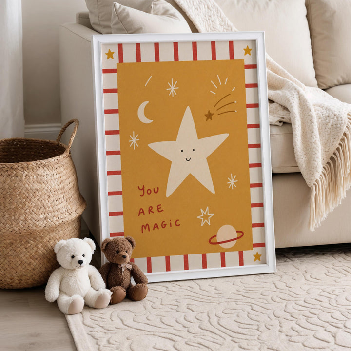 A framed poster with a star and a message is displayed on a wall, accompanied by two stuffed teddy bears sitting on the floor next to a woven basket.