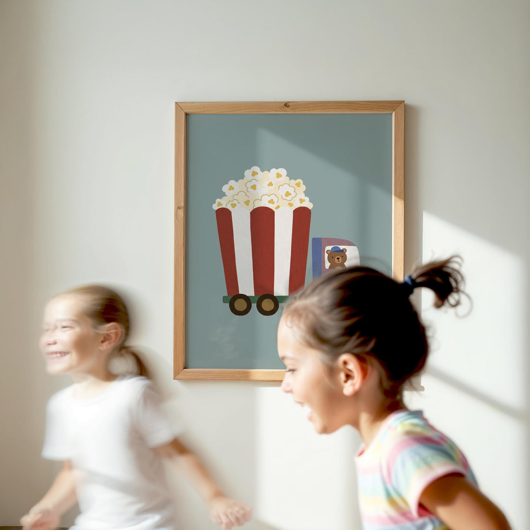 Two young girls are running in a room, with a framed picture of a popcorn cart hanging on the wall behind them.