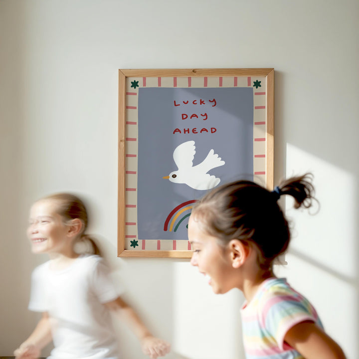 Two young girls are running in front of a framed poster with a bird and a rainbow, which says "Lucky Day Ahead".