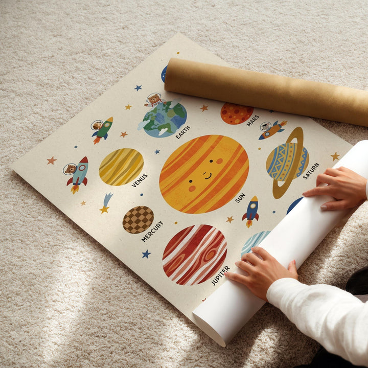 A child's hands are seen rolling up a poster depicting a solar system, with various planets and stars illustrated on it.