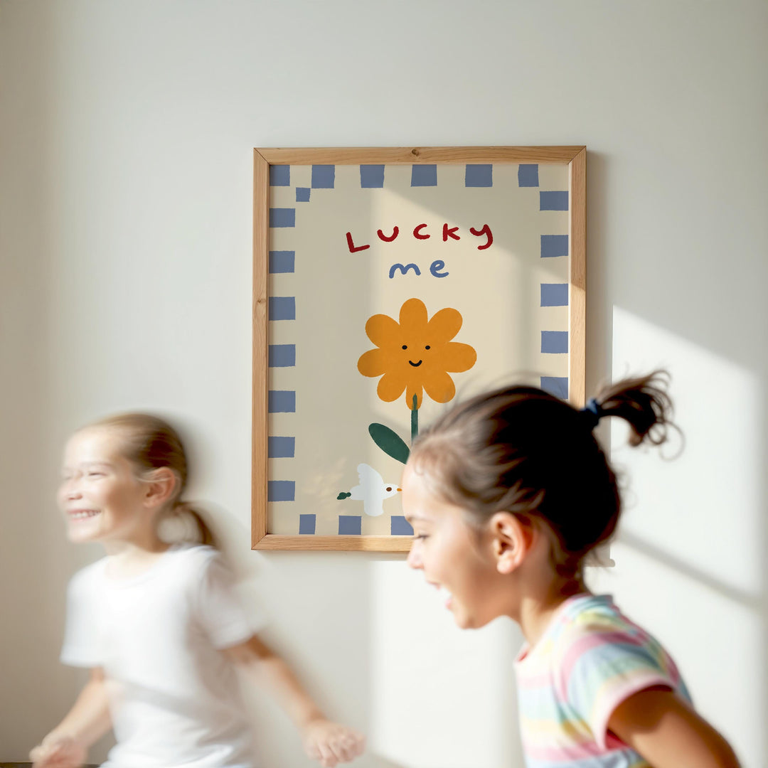 Two young girls are running in a room with a framed poster of a flower and the word "Lucky me" on the wall.