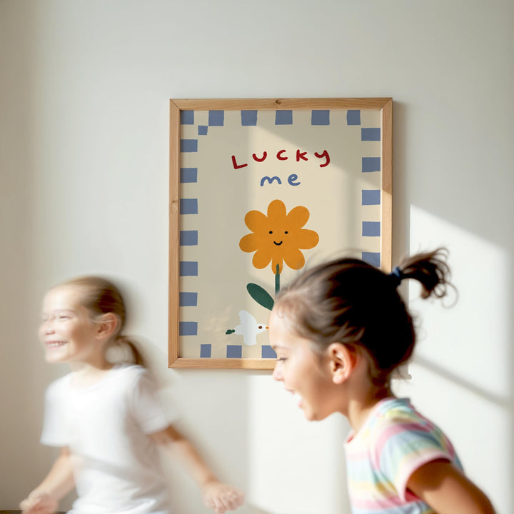 Two young girls are running in a room with a framed poster of a flower and the word "Lucky me" on the wall.