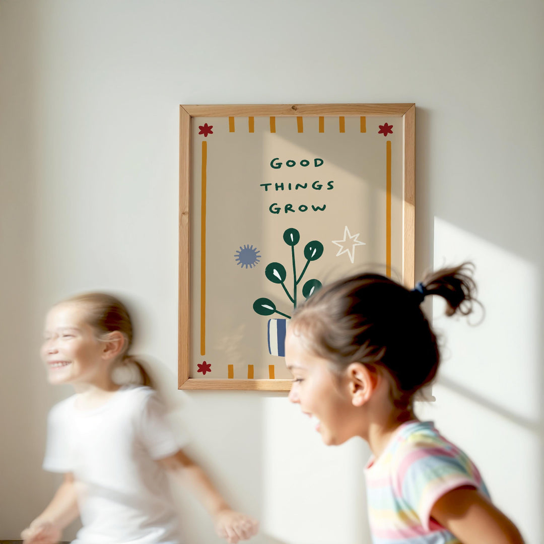 Two young girls are running in front of a framed poster with the text "Good things grow" and a plant illustration.