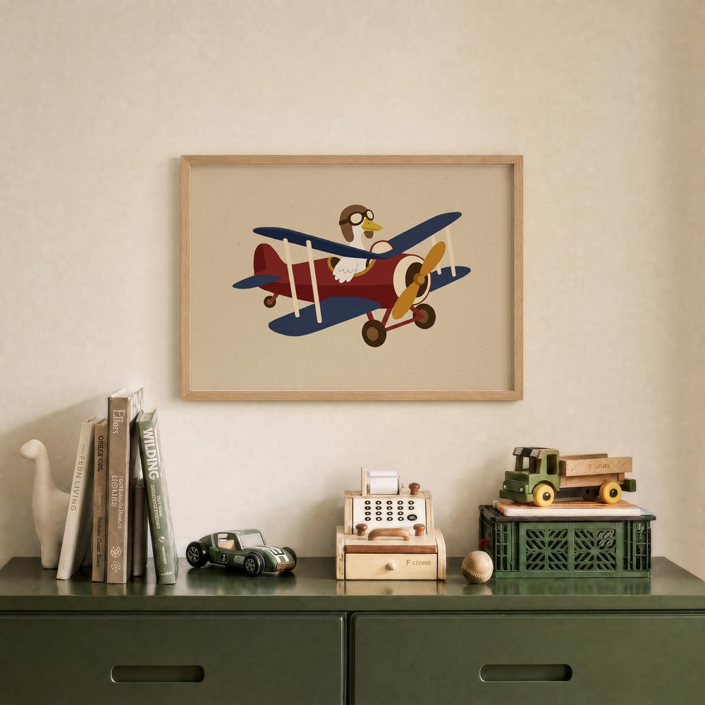 a framed illustration of a red and blue biplane with a cartoon character on it, hanging on a wall above a green dresser with various toys and books on it.