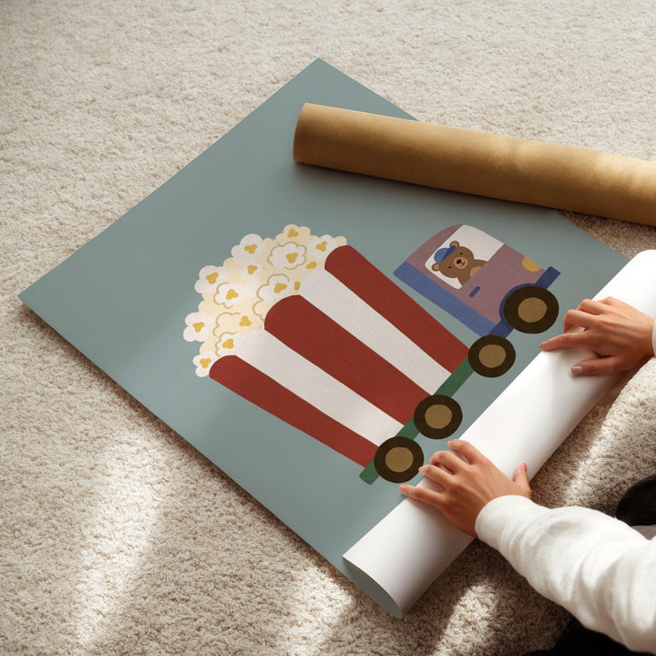 A child's hands are holding a roll of paper, which appears to be a piece of artwork depicting a train with a red and white striped car and a cartoon bear.