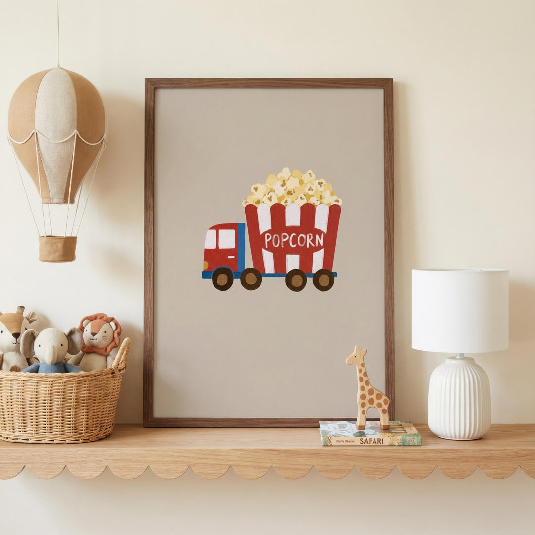 a framed poster of a red and white popcorn truck with the word "POPCORN" on it, placed on a shelf next to a lamp and a basket of stuffed animals.