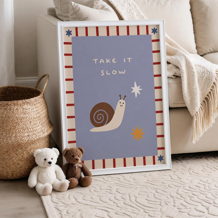 a framed poster with a snail and a star, placed on a carpeted floor next to a white couch. There are two teddy bears sitting on the floor in front of the poster.