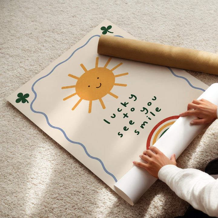 A child's hands are seen rolling up a poster with a sun and rainbow design, along with the text "lucky see you smile".