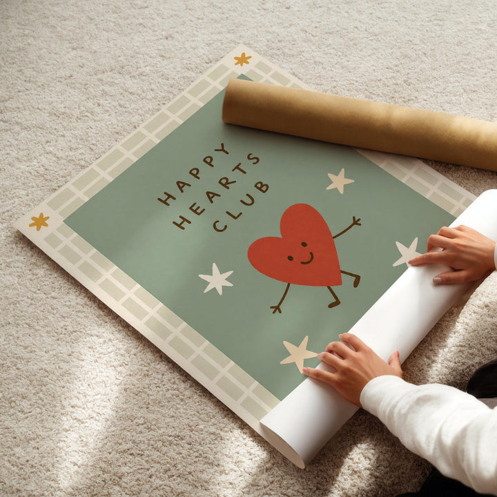 A person's hands are rolling up a poster with a heart and stars design, which appears to be part of the "Happy Hearts Club" project.
