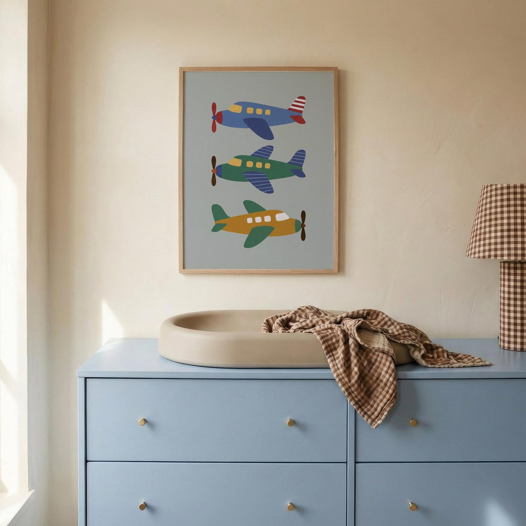 a blue dresser with a beige changing pad on top, and a framed poster of colorful airplanes hanging on the wall above it.