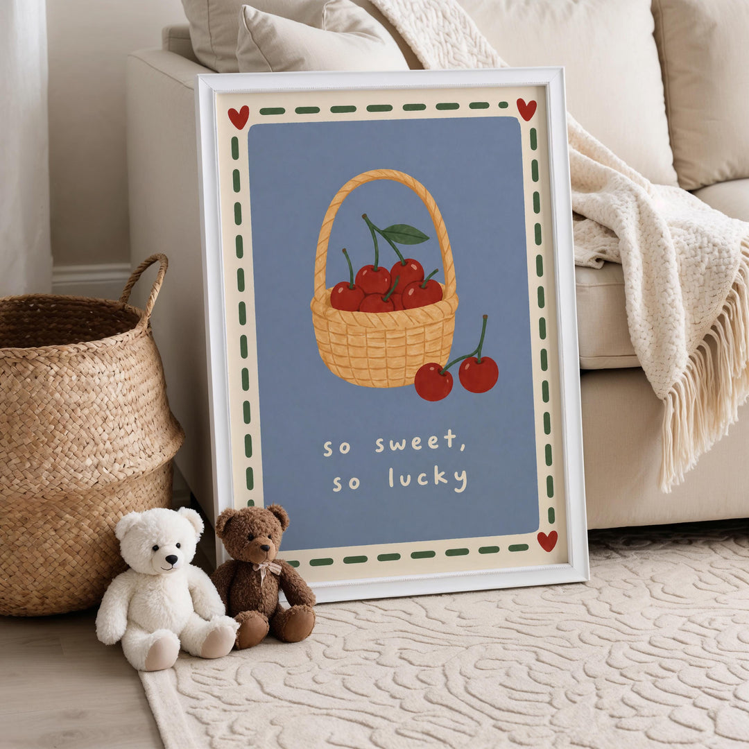 A framed illustration of cherries in a basket is displayed on a wall, accompanied by two stuffed teddy bears sitting on the floor next to a woven basket.