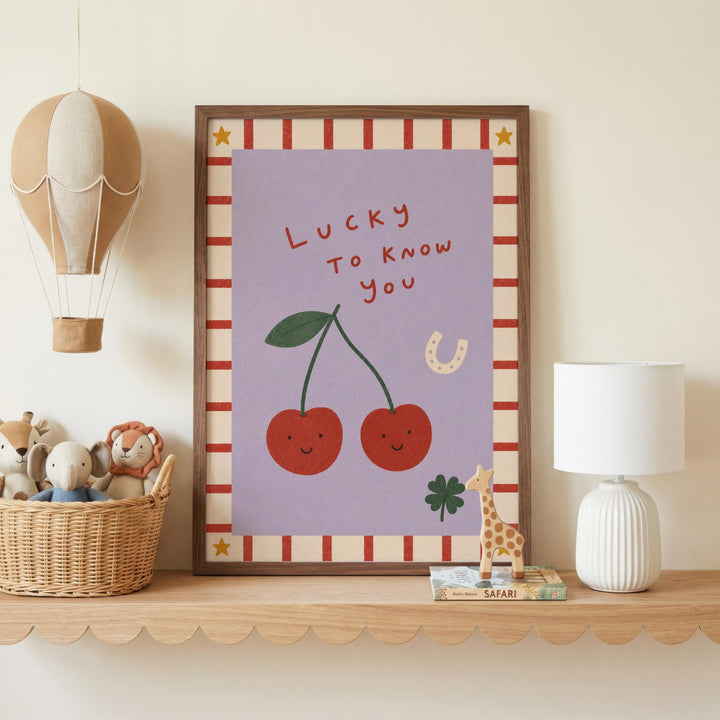 a framed poster with a cartoon illustration of cherries and a message that says "Lucky to know you". The poster is displayed on a shelf, along with a hot air balloon, a lamp, and some stuffed animals.