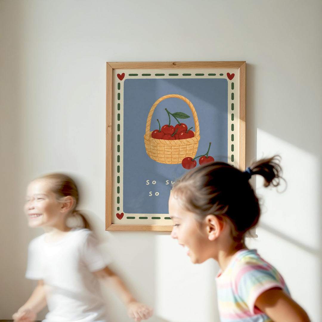 Two young girls are running in front of a framed picture of cherries on a wall.